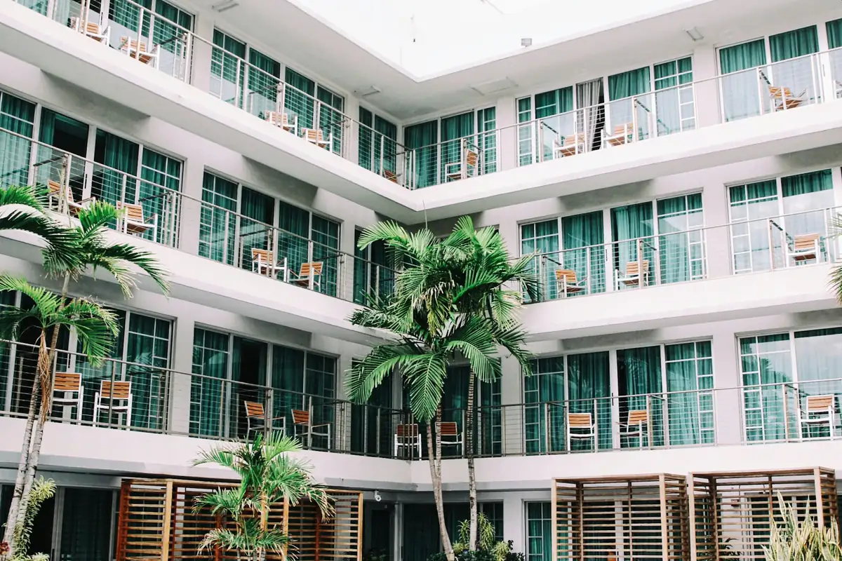 White multi storey hotel with balconies wrapped around a palm planted courtyard
