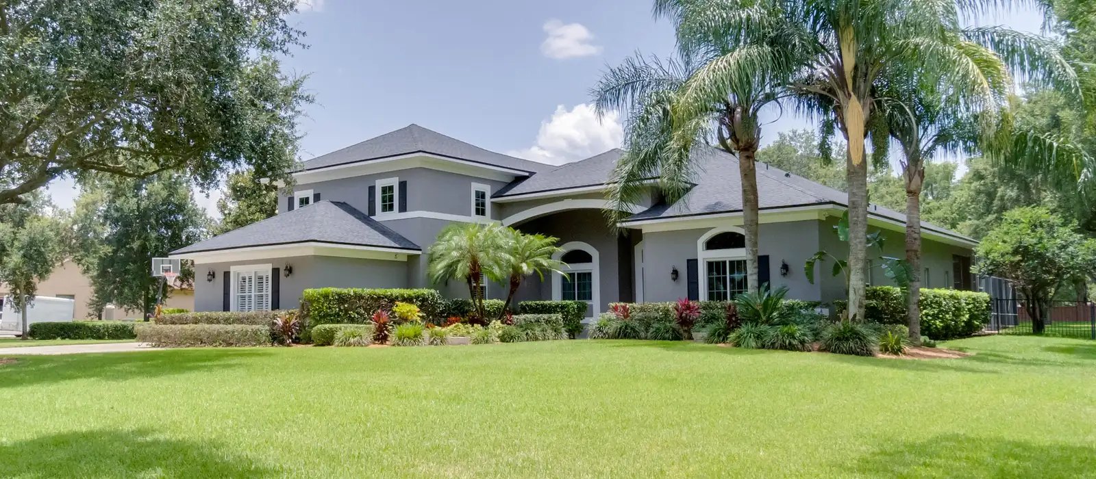 Two storey gray home framed by palm trees and a live oak on a wide lawn in Windermere