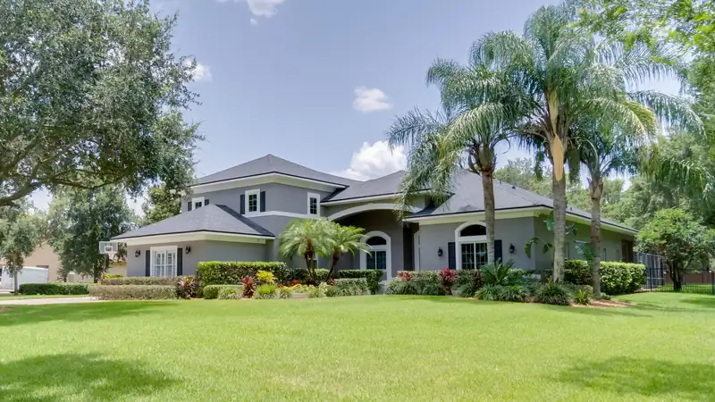 Two storey gray home framed by palm trees and a live oak on a wide lawn in Windermere